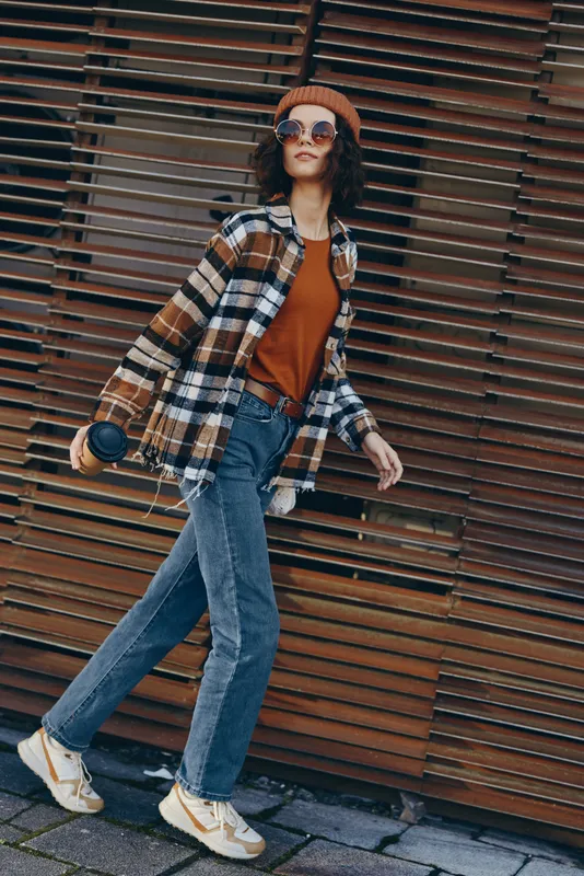woman walking urban fashion casual sunglasses beanie plaid in city street, candid lifestyle with authenticity and golden hour glow, mindful living and emotional storytelling.