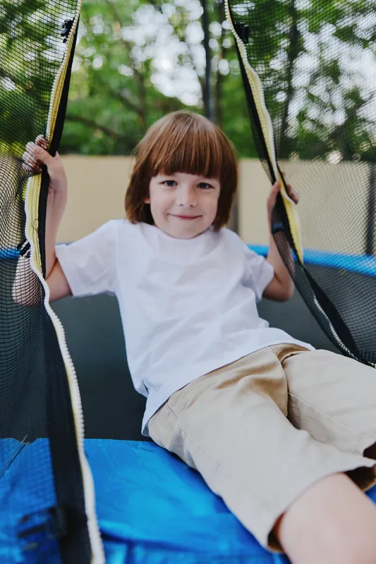 Cheerful boy playing on a trampoline, enjoying the outdoors with vibrant greenery in the background. A fun and playful moment captured in motion.