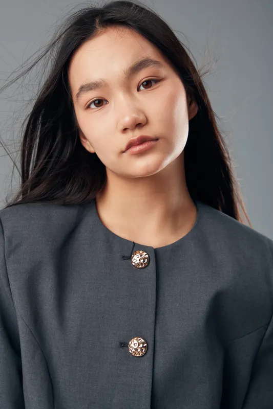 Young woman with long dark hair wearing a gray buttoned shirt in studio. Closeup portrait with natural expression and soft lighting on neutral background for beauty and fashion.