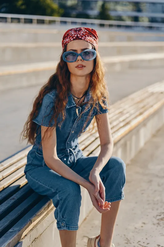 Lifestyle woman in modern boho-western denim street style wearing sunglasses and red bandana, captured in warm film color tones outdoors on sunny day.