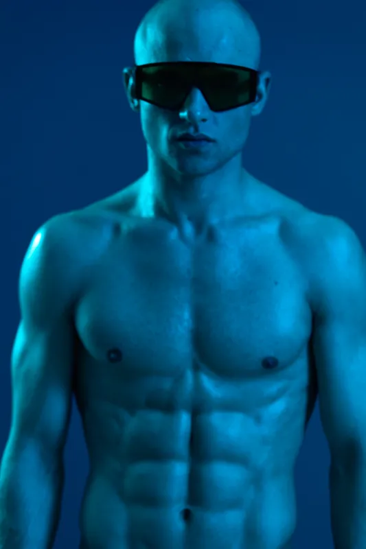 Powerful man showcasing a strong physique, wearing sunglasses, captured in a vibrant blue hue that emphasizes his muscular form and striking presence.