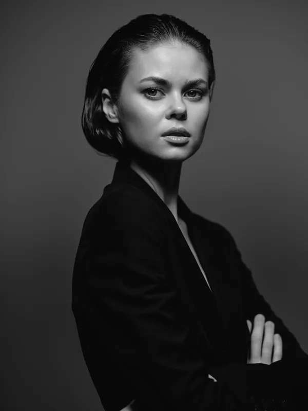 Black and white portrait of a serious young woman wearing a dark jacket with folded arms in a studio setting