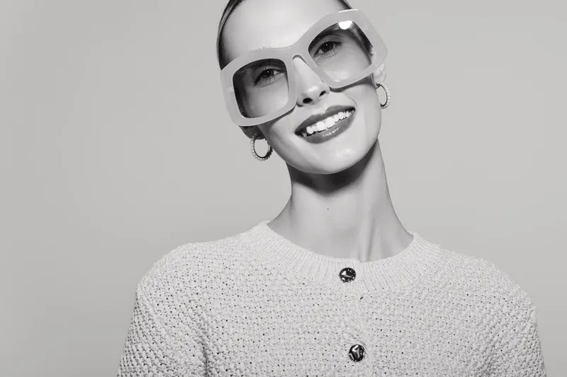 Smiling Caucasian woman with fair skin in oversized sunglasses and textured top poses with confident happy expression.