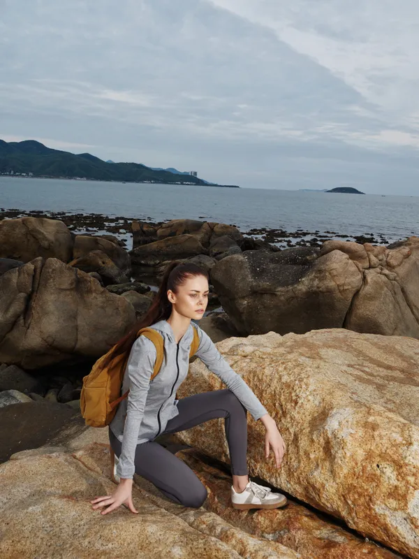 Young woman in sporty attire on rocky beach, showcasing determination and adventure spirit while enjoying nature s beauty and seeking a healthy lifestyle