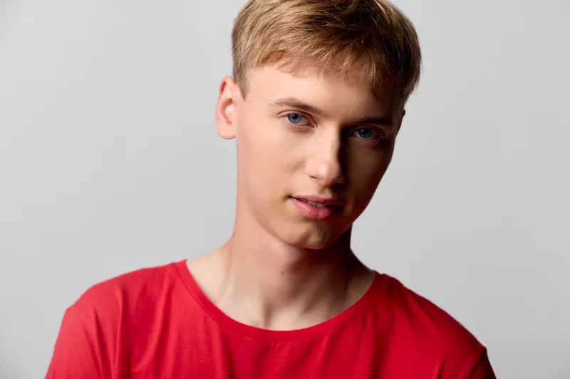 Young man in a red shirt with a calm expression, captured in studio style with soft lighting, clean background, and a modern pose for a contemporary fashion image