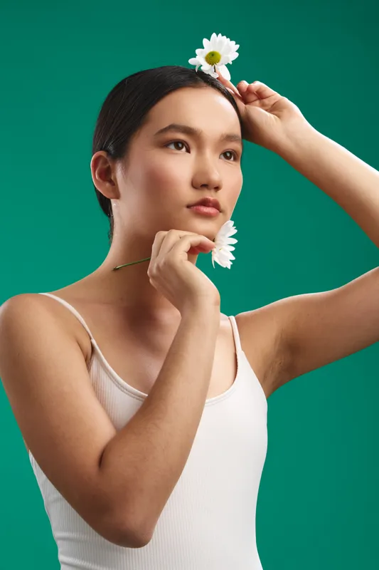 asian woman portrait in studio with flower accessory, calm expression and soft lighting, minimal fashion vibe conveying poise, elegance, and contemporary beauty.