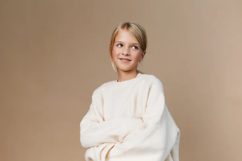Authentic portrait of a young girl in a cozy sweater, celebrating everyday play and school life with natural light, candid pose, and gentle charm.