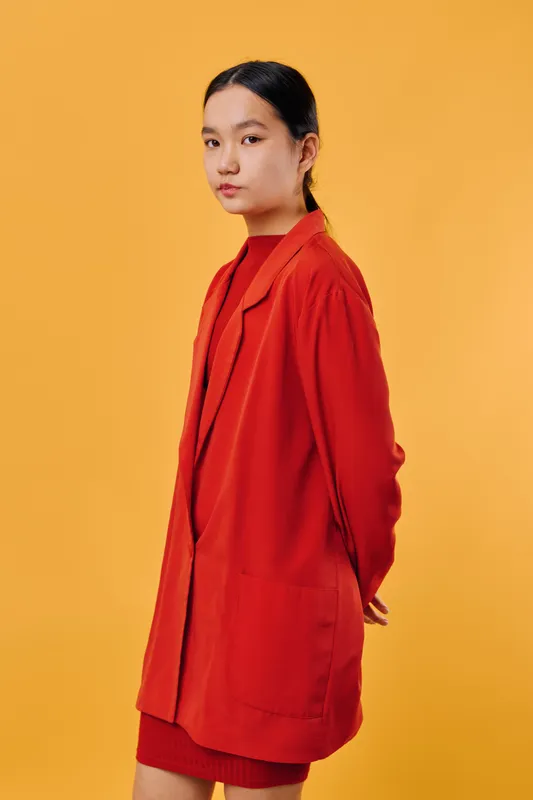 Young woman wearing red jacket and red dress standing against yellow background. Portrait of confident female fashion model with casual hairstyle and serious expression in studio.