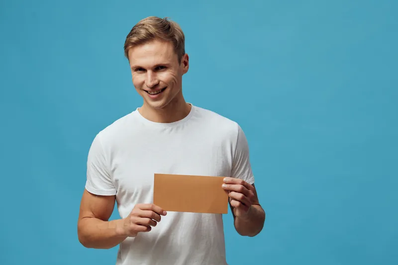 Smiling happy young caucasian man hold blank envelope in hands wear white t-shirt on blue background digital detox concept