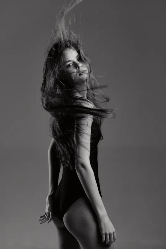 Black and white portrait of a woman with flowing hair wearing a dark swimsuit, expressing elegance and motion.