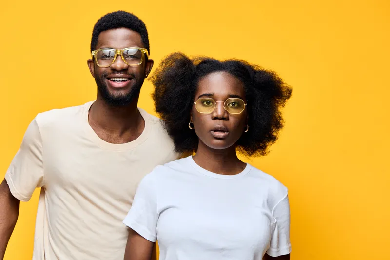 Happy African American couple with stylish glasses on a bright yellow background, showcasing joy and confidence in a vibrant summer fashion style