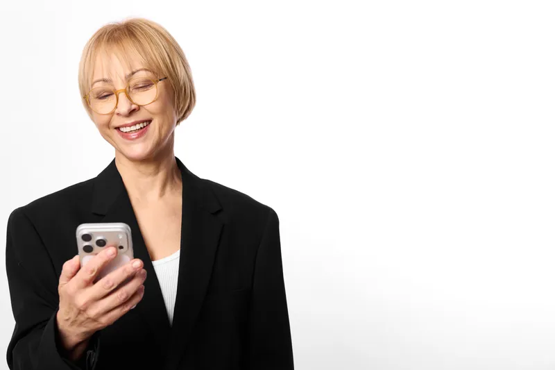 Smiling senior businesswoman holds smartphone in studio, white background, relaxed portrait, visible hands, mobile communication and technology concept, copy space