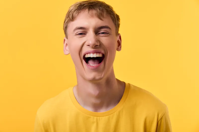 Laughing man wearing a yellow shirt against a bright yellow backdrop, expressing joy and cheer. Studio shot focusing on bold color, lively mood, and positive energy.