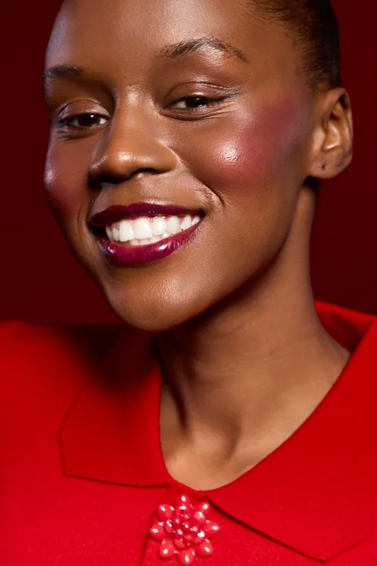 Close-up portrait of happy African woman with dark skin smiling confidently wearing red clothing on red background. Concept for beauty, fashion, and positive emotions in studio lighting.