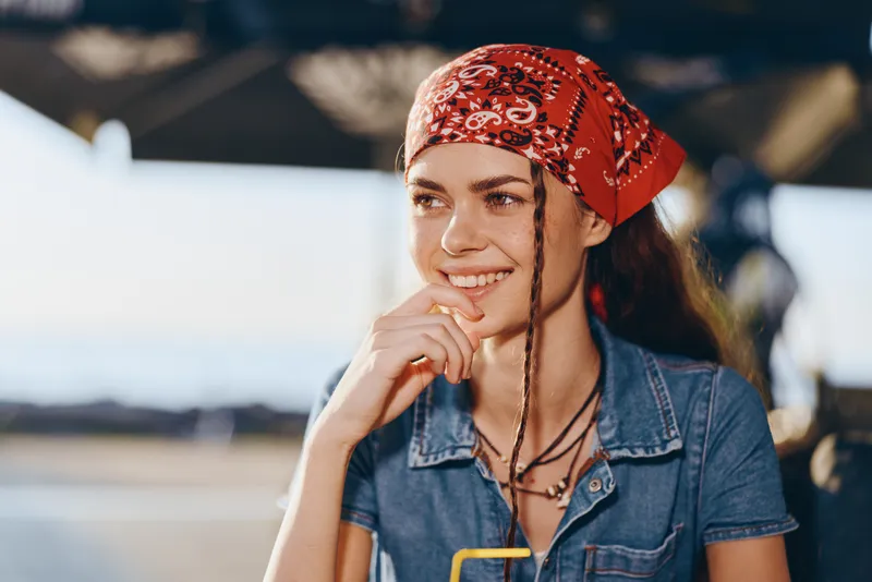 lifestyle woman in modern boho-western denim street style with red bandana smiling outdoors in film color tone, casual summer look, natural light