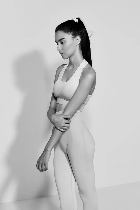 Sport fitness woman in athletic wear standing in profile with thoughtful expression, minimalist background, black and white portrait conveying strength and focus.