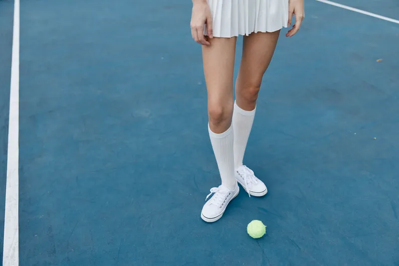 Young woman in white tennis outfit standing on blue court with tennis ball, showcasing athleticism and style, perfect for sports and fitness themes