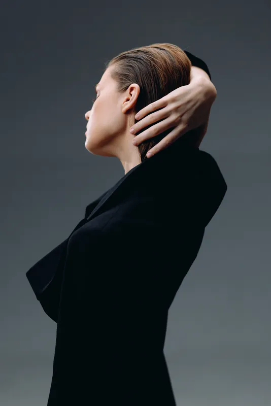 Elegant woman in black outfit posing against a dark background with a serene expression and minimalistic style.