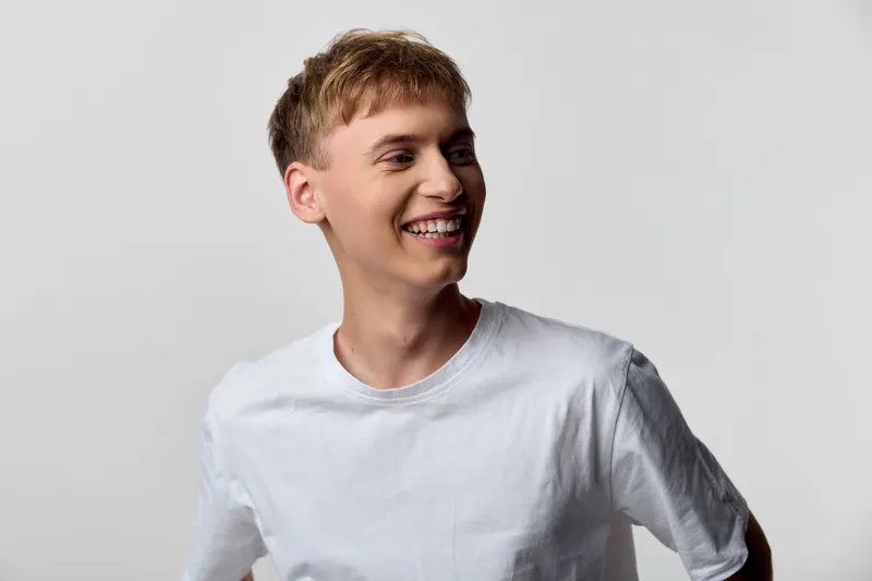 Man with a bright smile wearing a white t-shirt in a studio, showcasing casual style, joyful energy, and relaxed confidence for lifestyle, fashion, and advertising projects