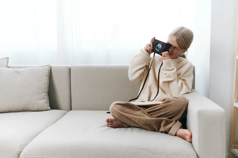Authentic candid scene of a student on a cozy sofa, capturing moments with a camera, embracing a simple lifestyle and school life themed play in a calm home setting.