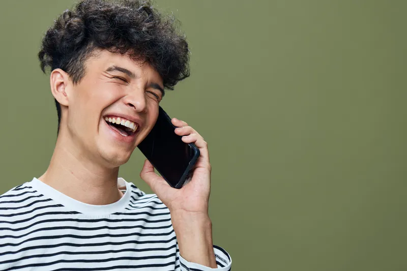 laughing man talking phone young casual curly hair striped shirt green background bright emotion