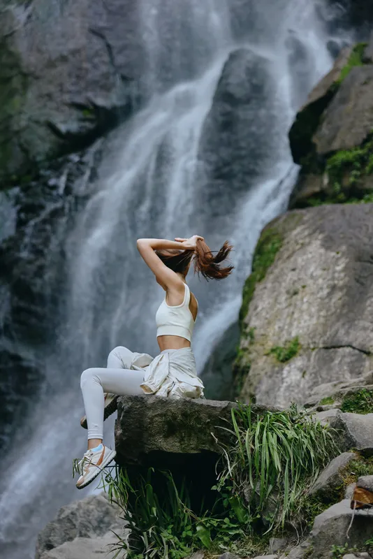 woman sitting waterfall wearing white activewear tying hair outdoor nature fitness lifestyle wellness healthy exercise motion