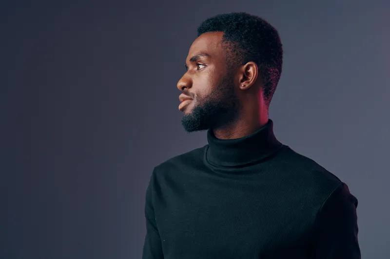 Portrait of a young Black man wearing a black turtleneck, showcasing confidence and introspection against a gradient background in muted tones