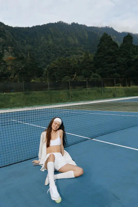 Young woman in tennis attire expressing joy on the court, showcasing athleticism, sports fashion, and natural beauty in a vibrant outdoor setting