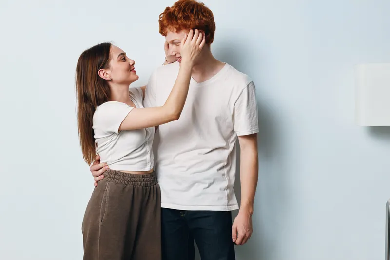 Couple, woman and man standing close with affectionate gesture, smiling and touching face in casual clothes for love, relationship and tender moment at home.