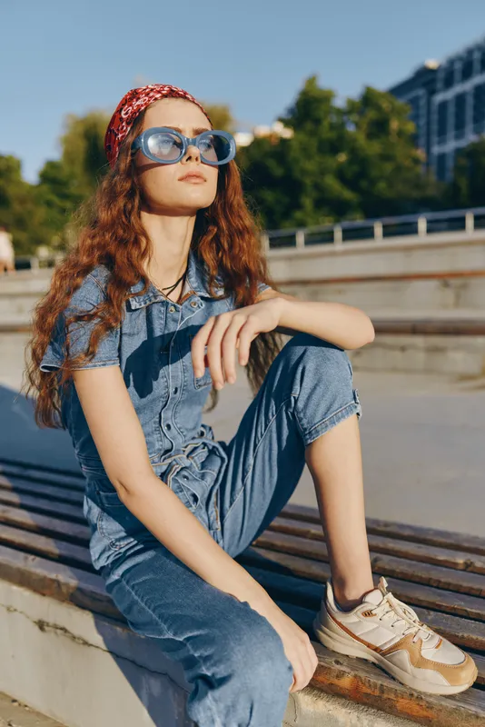 lifestyle woman in modern boho-western denim street style wearing sunglasses and a red bandana, outdoors with urban background, film color effect