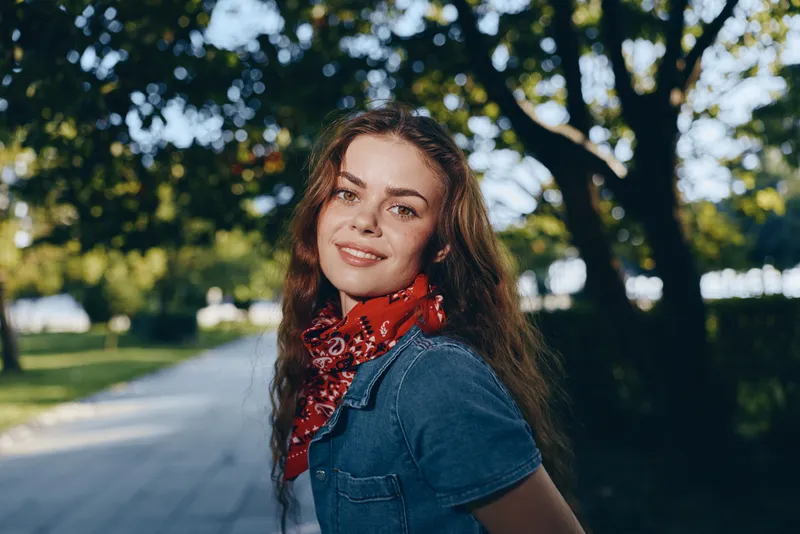 lifestyle woman in modern boho-western denim street style with film color effect smiling outdoors in park surrounded by trees in warm natural sunlight