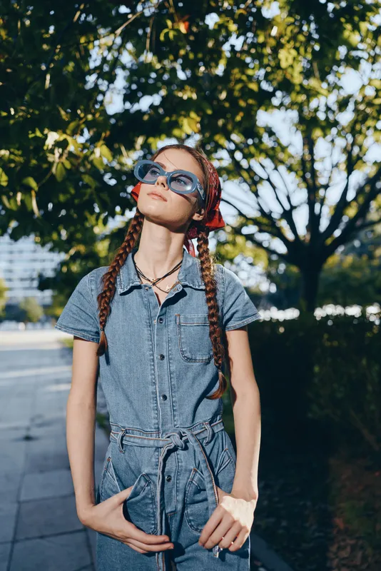 modern boho-western denim street style woman wearing sunglasses and braided hair enjoying sunny day outdoors in urban lifestyle setting with vibrant film color tones