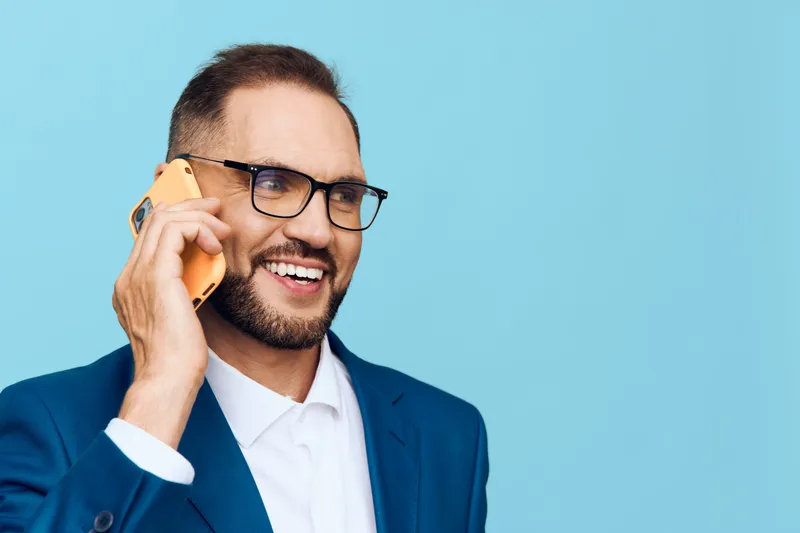 A professional man in a blue suit speaks on a mobile phone against a solid blue backdrop, conveying confident communication and a positive business mood.