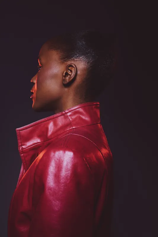 Profile of a black woman with dark skin wearing a red leather jacket. The image shows side view on black background. Fashion concept with afro hairstyle and modern style.