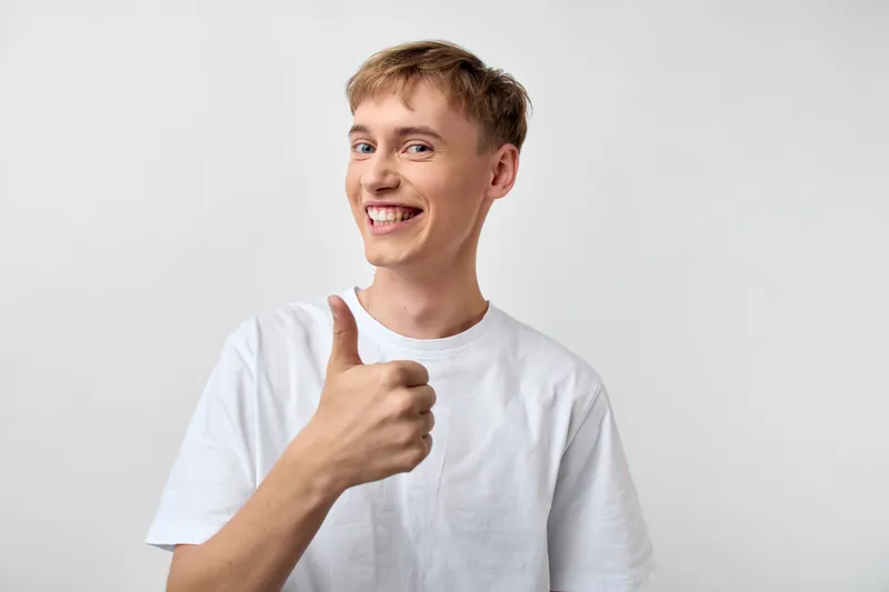 Happy young man gives a thumbs up in a casual pose, conveying positivity, confidence and friendly approval in a clean, well lit studio setting suitable for lifestyle or marketing projects