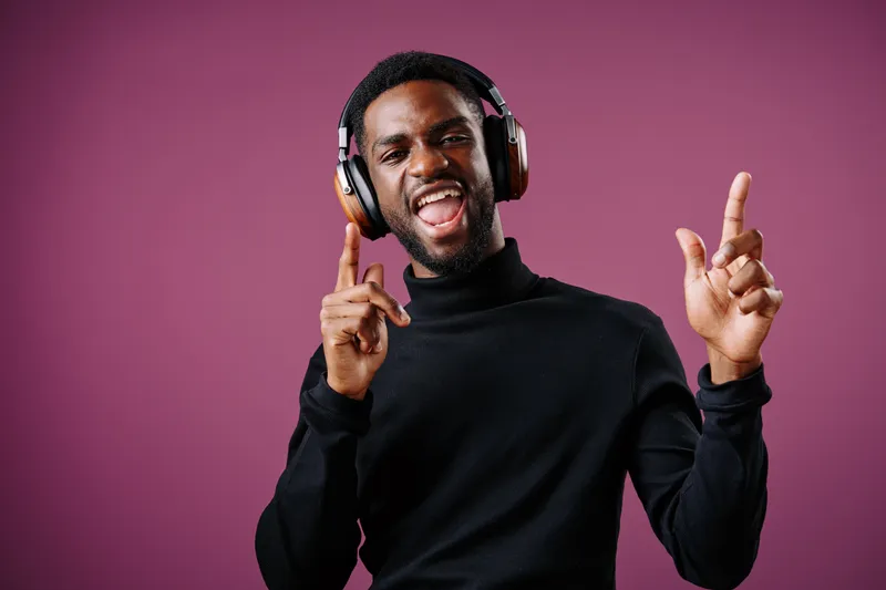 Smiling young Black man enjoying music with headphones, expressing happiness and joy against a vibrant purple background