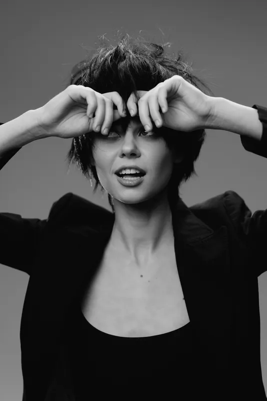 Black and white portrait of a smiling woman with short hair wearing a dark jacket and expressive pose.