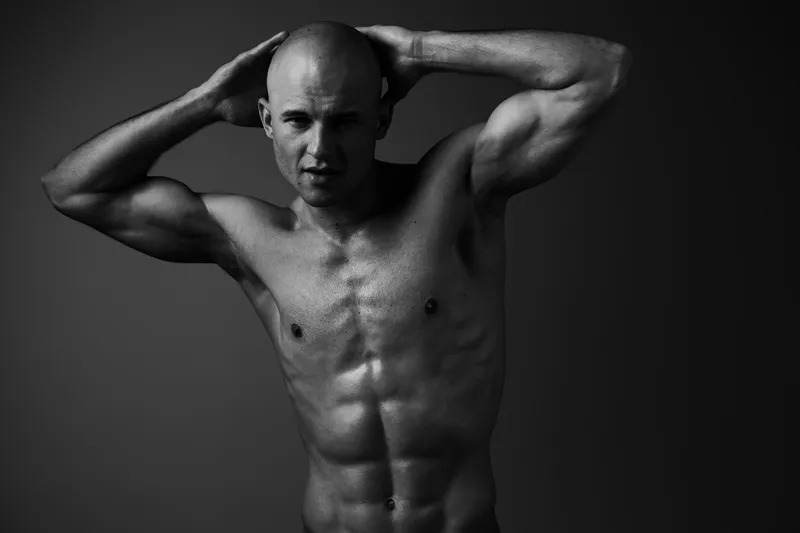 Black and white image of a muscular man posing confidently, showcasing strength and determination with a striking expression, ideal for fitness inspiration.