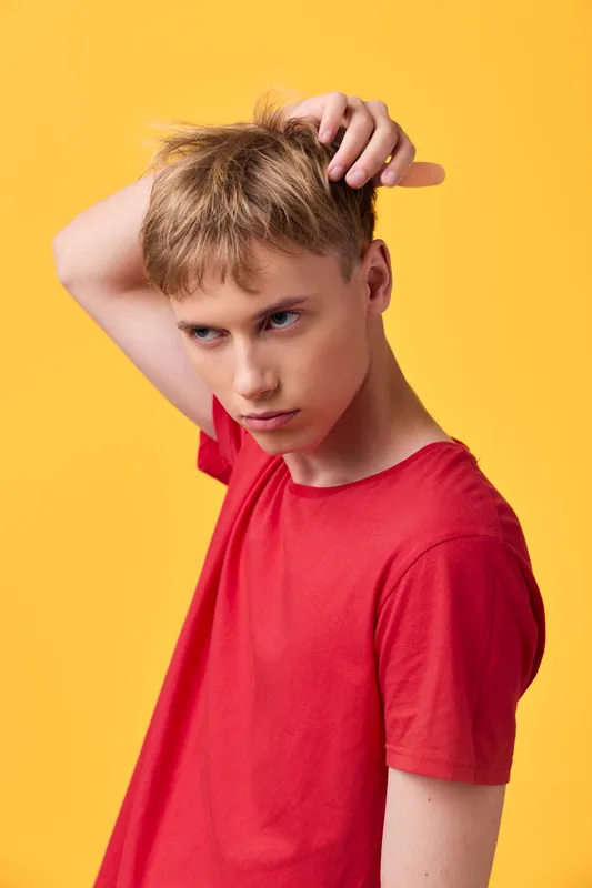 Male, young, scratching head, puzzled expression in a red shirt against bright yellow background, conveying curiosity, casual mood, fashion pose, studio lighting, clean composition