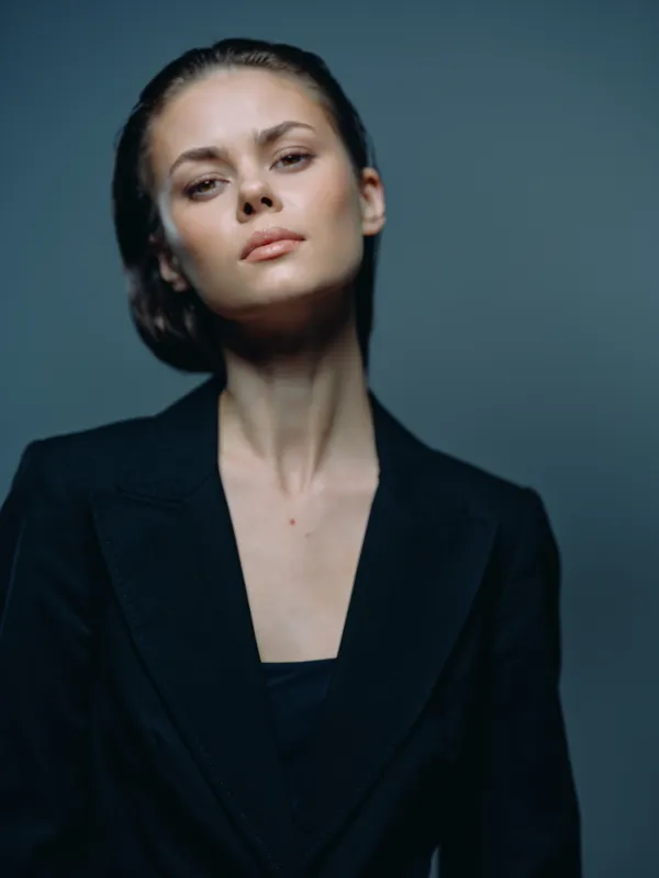 Elegant woman with serious expression wearing black blazer on dark background, stylish and confident pose.