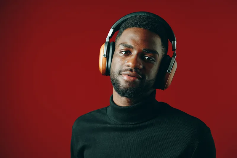 Confident young black man wearing stylish headphones against a vibrant red background, showcasing modern fashion and urban lifestyle trends