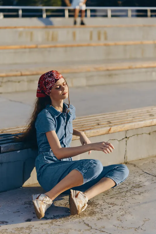 Lifestyle woman in modern boho-western denim street style relaxes outdoors with film color effect, embodying casual summer fashion and quiet confidence in urban setting.