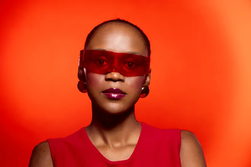 Portrait of confident black woman with dark skin wearing red sunglasses and sleeveless top against vivid orange background. Concept of fashion, style, and modern attitude.