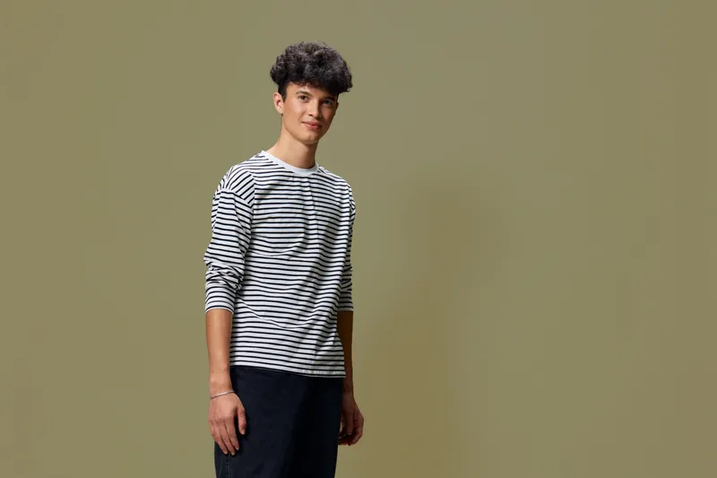 young man wearing striped shirt standing against plain olive background with relaxed posture and gentle expression, casual style, confident vibe