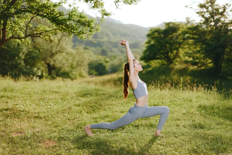Woman practicing yoga in a lush green field, wearing a gray athletic outfit, demonstrating strength and tranquility in nature