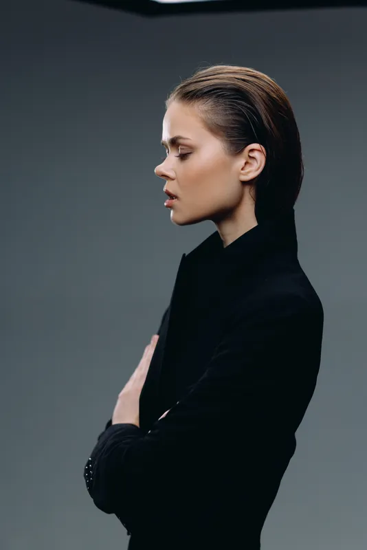Profile of a pensive young woman wearing a black turtleneck against a dark gray background.