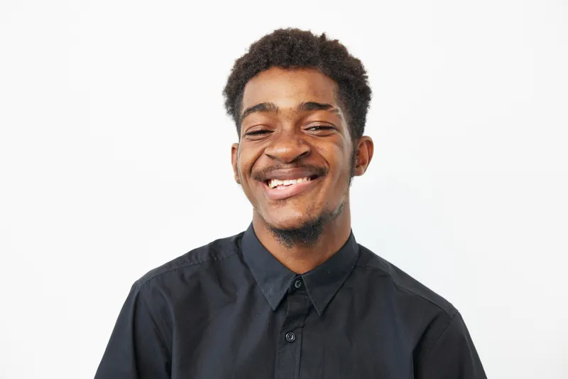 Joyful African American man smiling brightly, wearing a black shirt. His cheerful expression radiates positivity, making it perfect for promoting happiness and confidence.