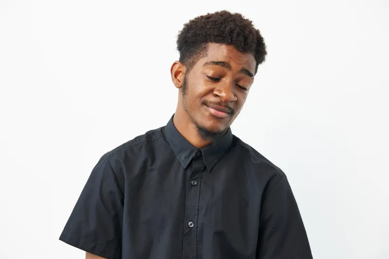 Black man with a relaxed expression, wearing a black shirt, exuding confidence and tranquility. Captivating portrait showcasing personality and style.