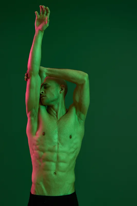 Athletic man posing dramatically in a captivating green light, showcasing strength and confidence with a focused expression and artistic background.