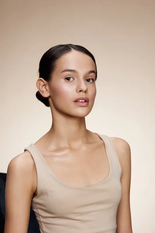 Beautiful female model with natural makeup, wearing a simple beige top, showcasing calm yet expressive emotions against a soft neutral background